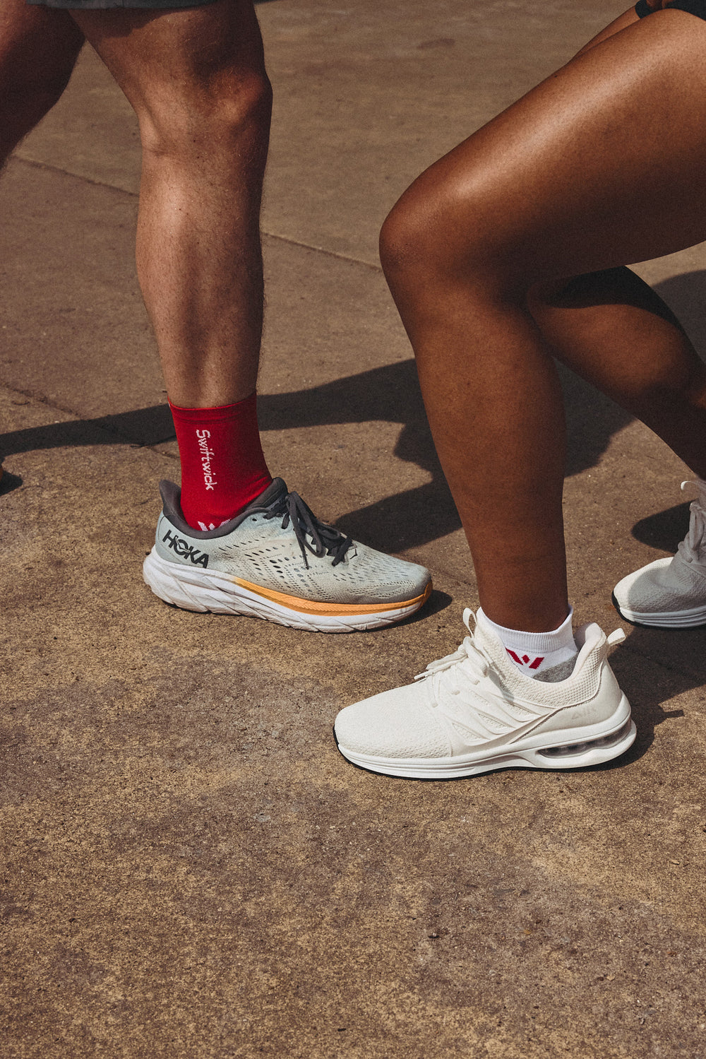 Close-up of two pairs of athletic shoes: grey HOKA and white Adidas.