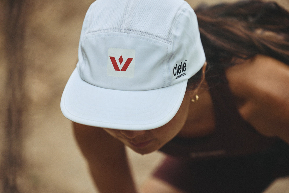A woman leaned over while wearing a white Swiftwick x Ciele running cap.