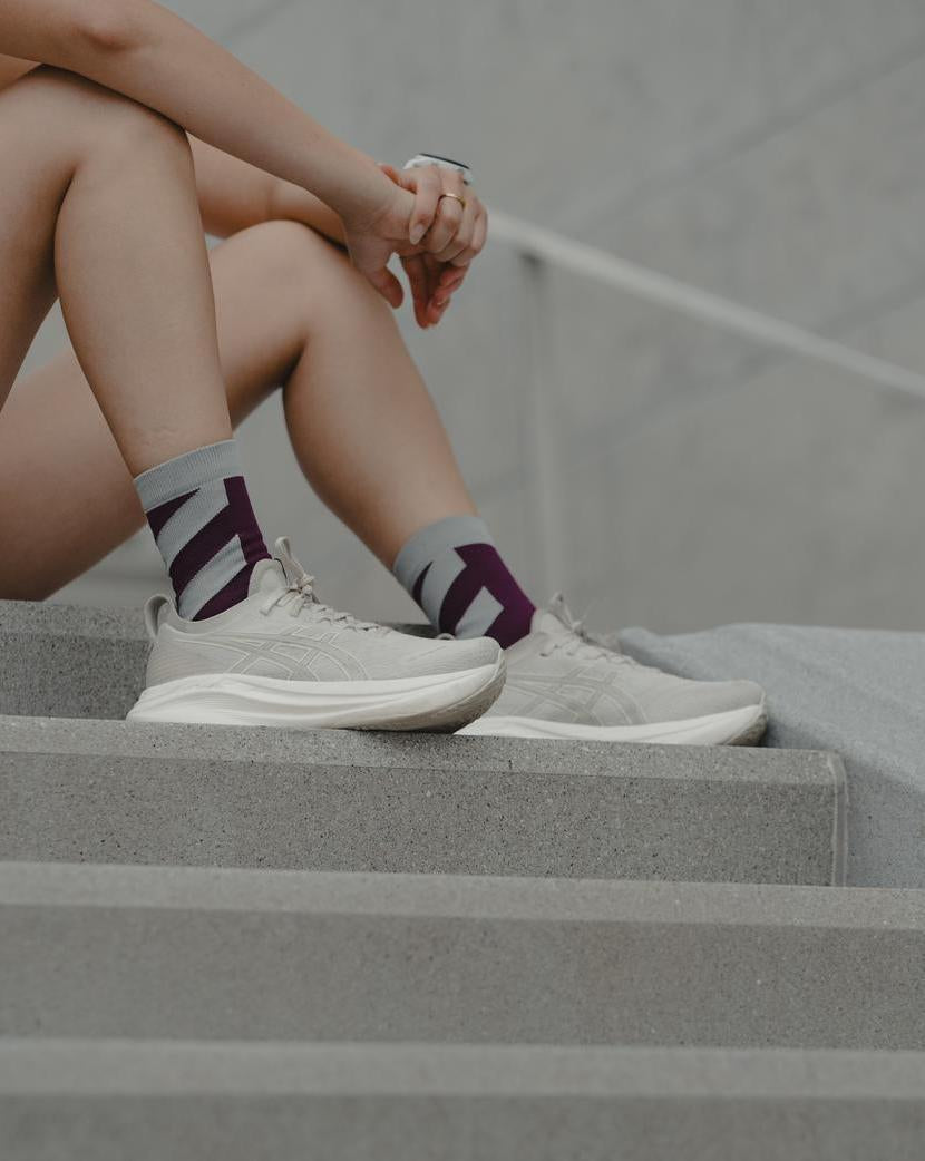 Person seated on steps wearing white Maxus Mid-Crew socks with burgundy details