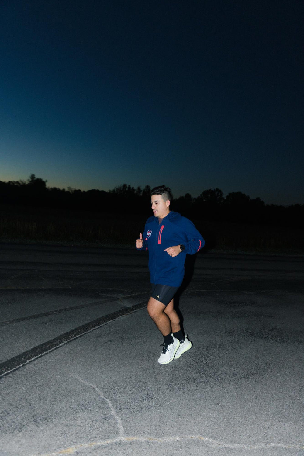 A person jogging on a road at night, wearing a blue hoodie and shorts.