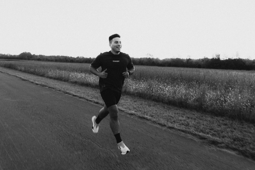 Runner smiling midstride on a paved country road with grassy fields and trees in the background