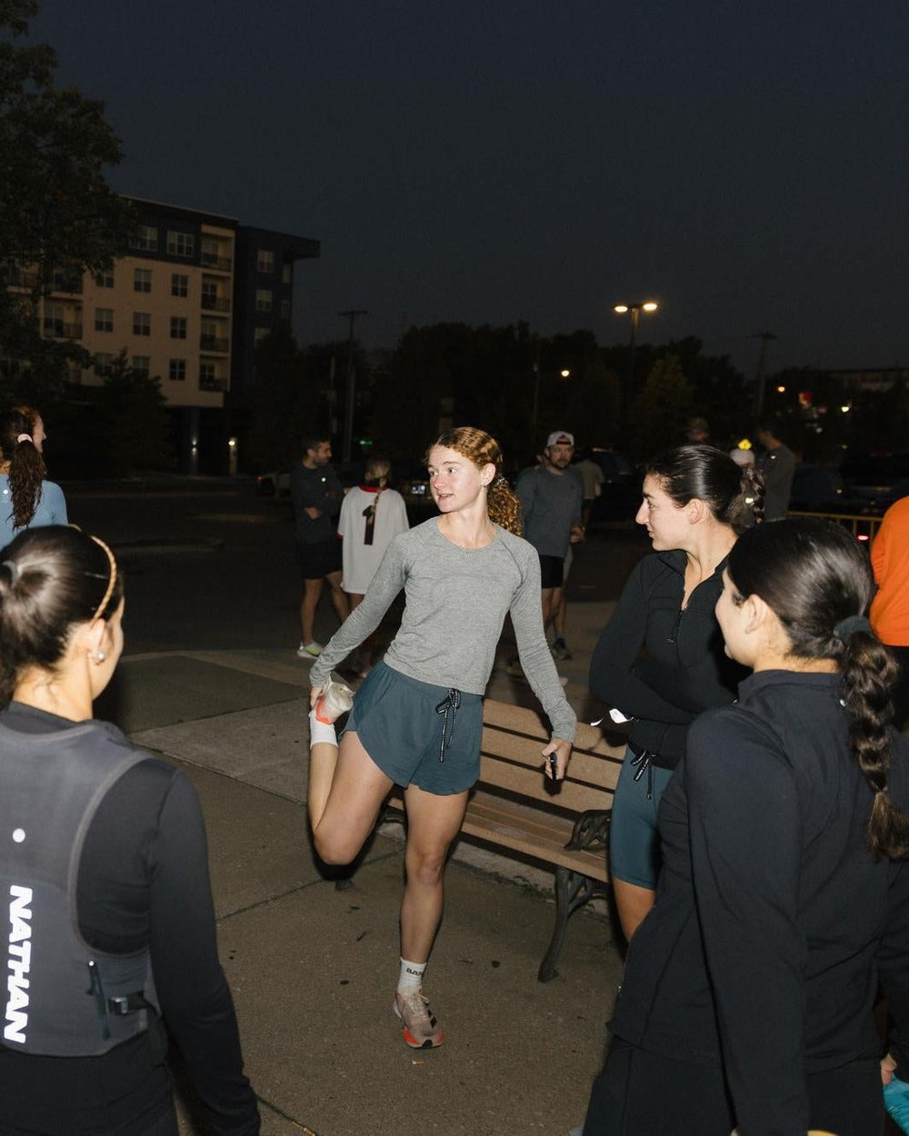 A group of women stretching before a run in an outdoor setting at dusk.