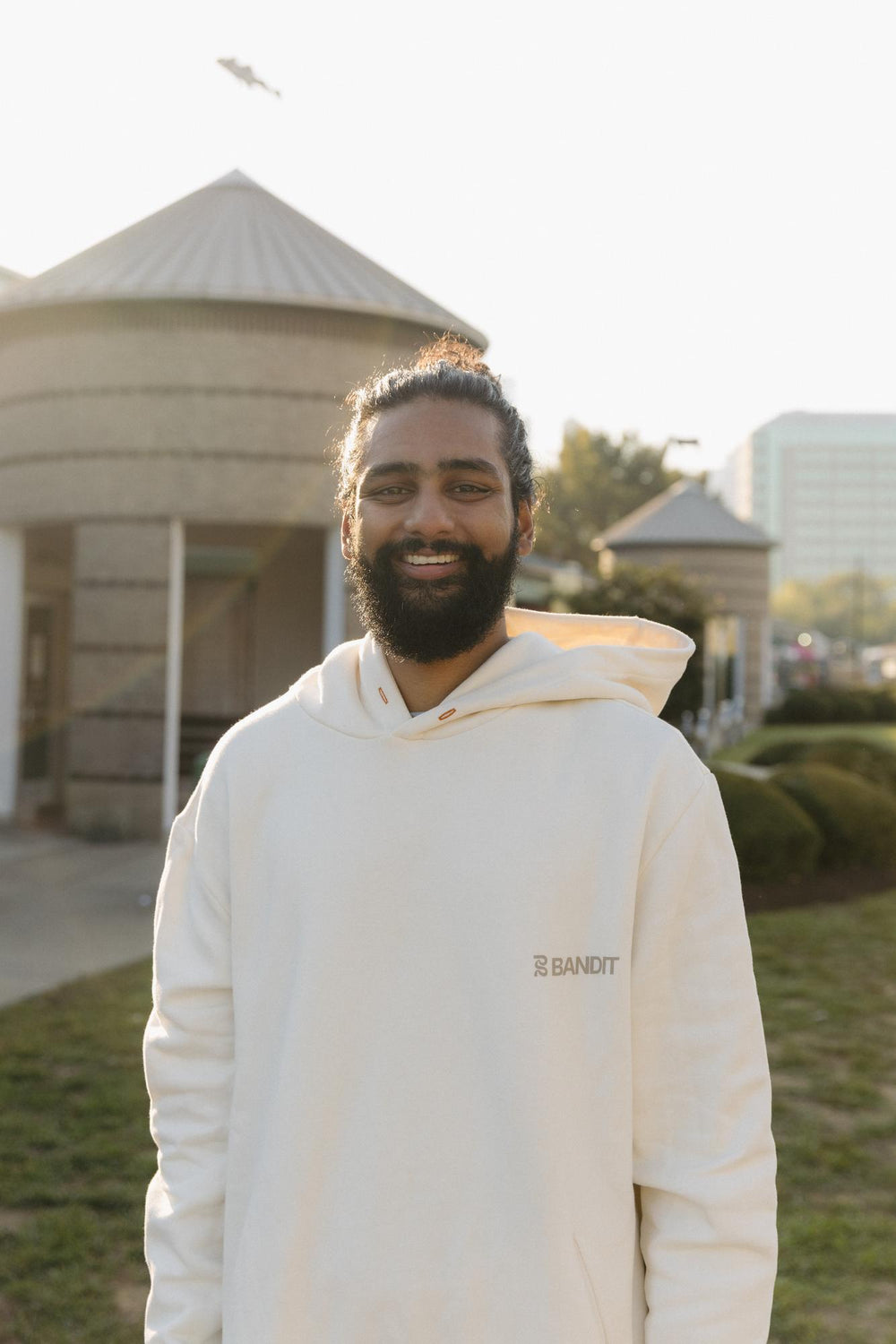 A person smiling outdoors wearing a white hoodie.