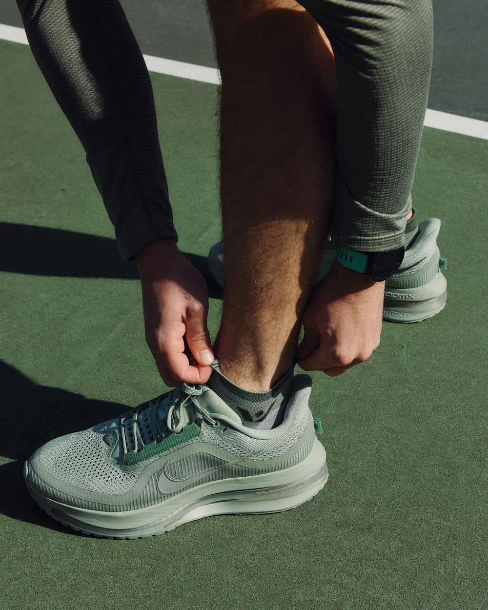 Runner adjusting green shoes while wearing Maxus No Show socks
