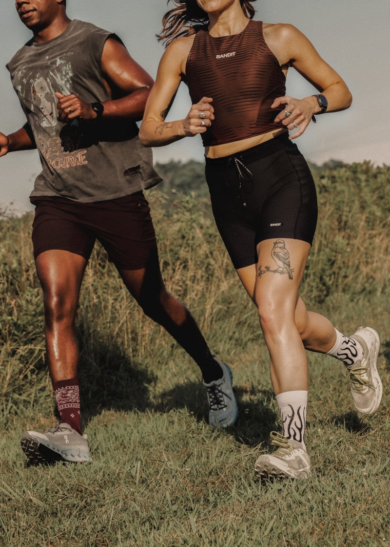 A man and woman running on a tree-lined street wearing Swiftwick Vision socks in the Bandana and Flames prints.