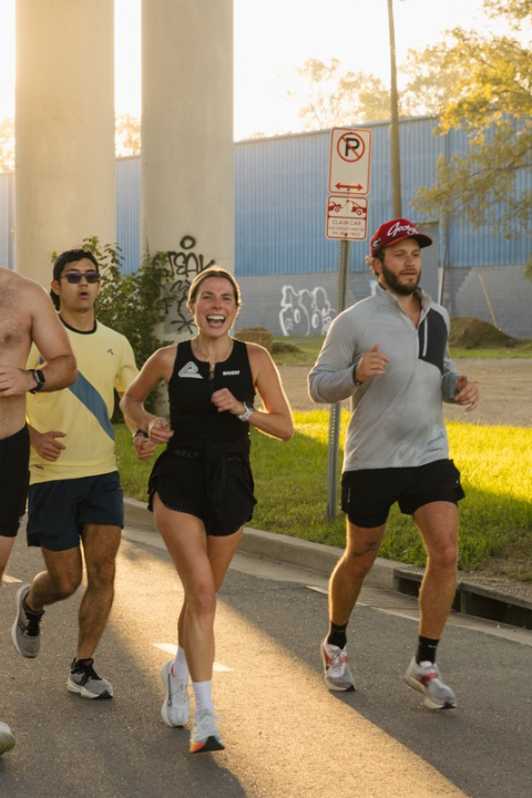A group of runners, including a smiling woman in the foreground, jogging on a street.