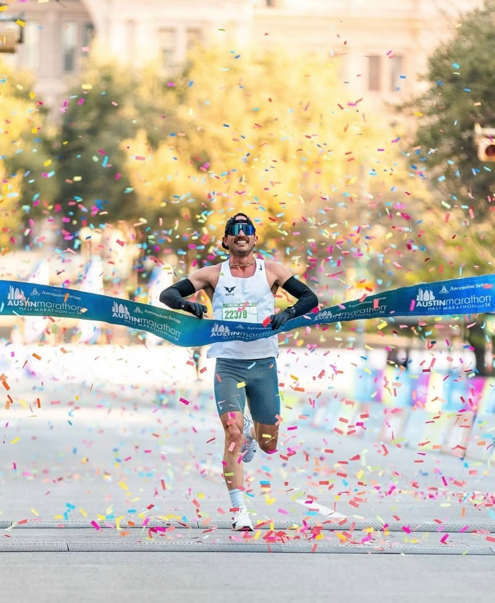 A runner crossing the finish line at the Austin Marathon, surrounded by colorful confetti.