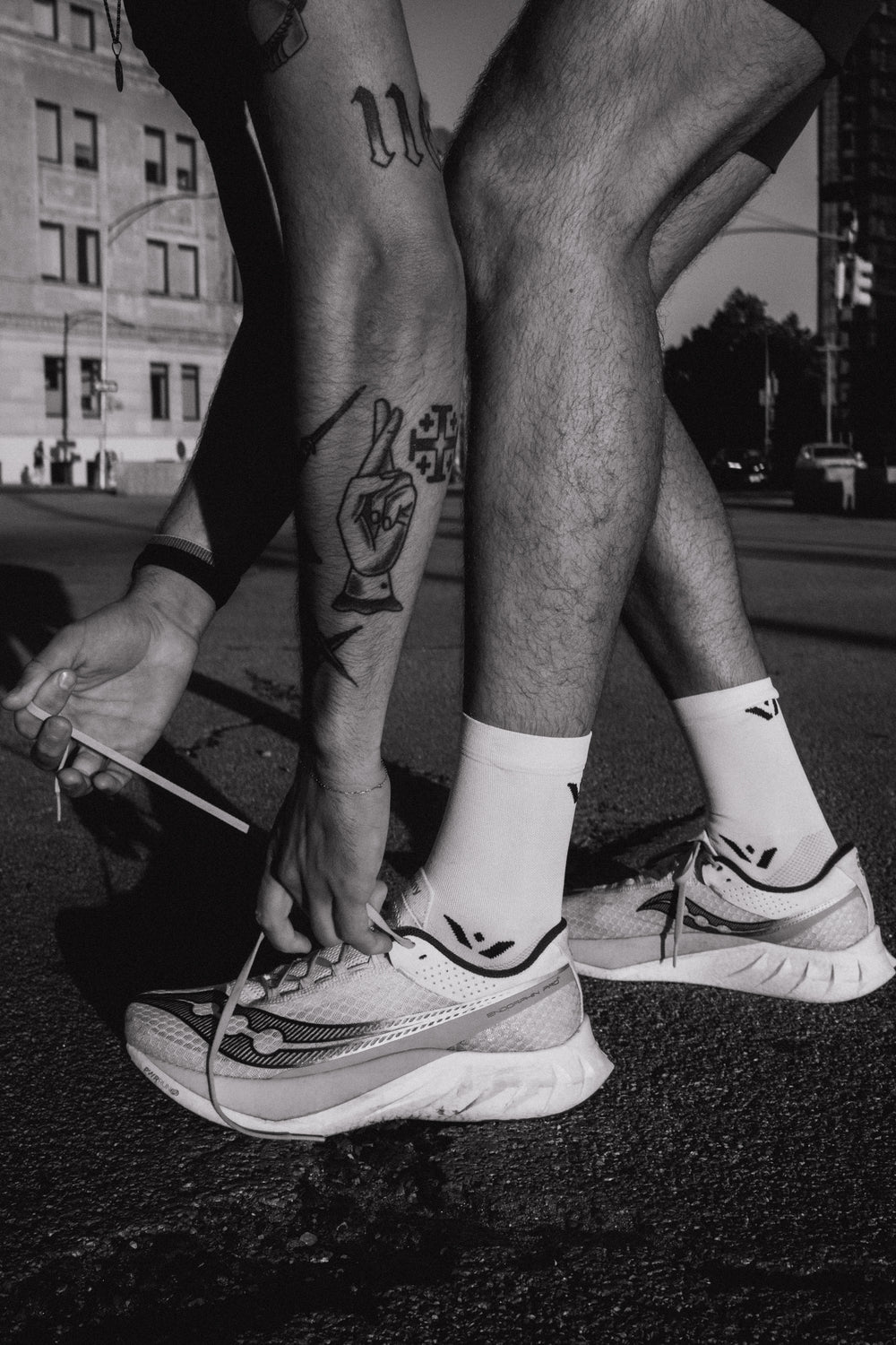 A person tying their shoelaces on athletic shoes, showing a tattoo on their leg.