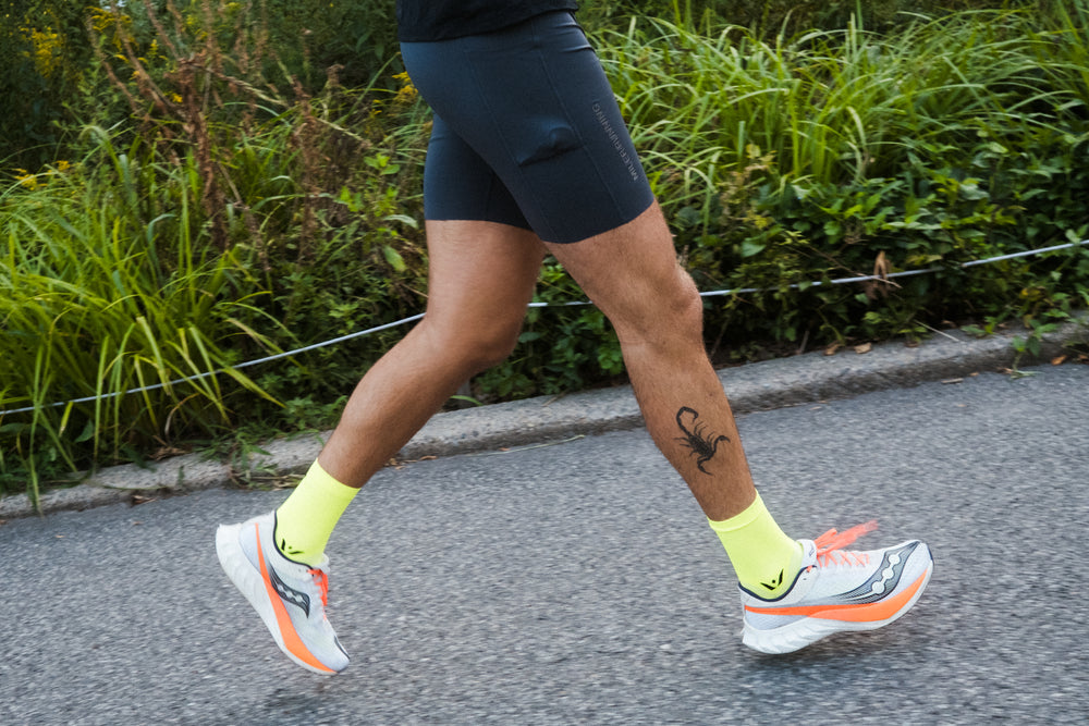 Side view of runner's lower legs wearing neon yellow ankle-length socks showcasing snug fit and cushioning on a paved path